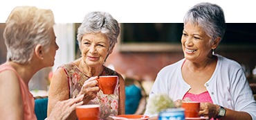 three elderly woman sitting down and having coffee together